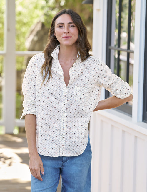 Woman wearing a white patterned shirt and blue jeans standing outdoors., view 3