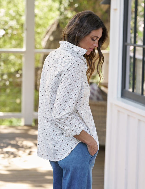 Woman wearing a white patterned shirt and blue jeans standing outdoors., view 4