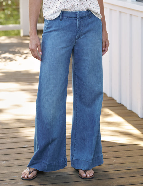Person wearing blue wide-leg jeans on a wooden deck, front view