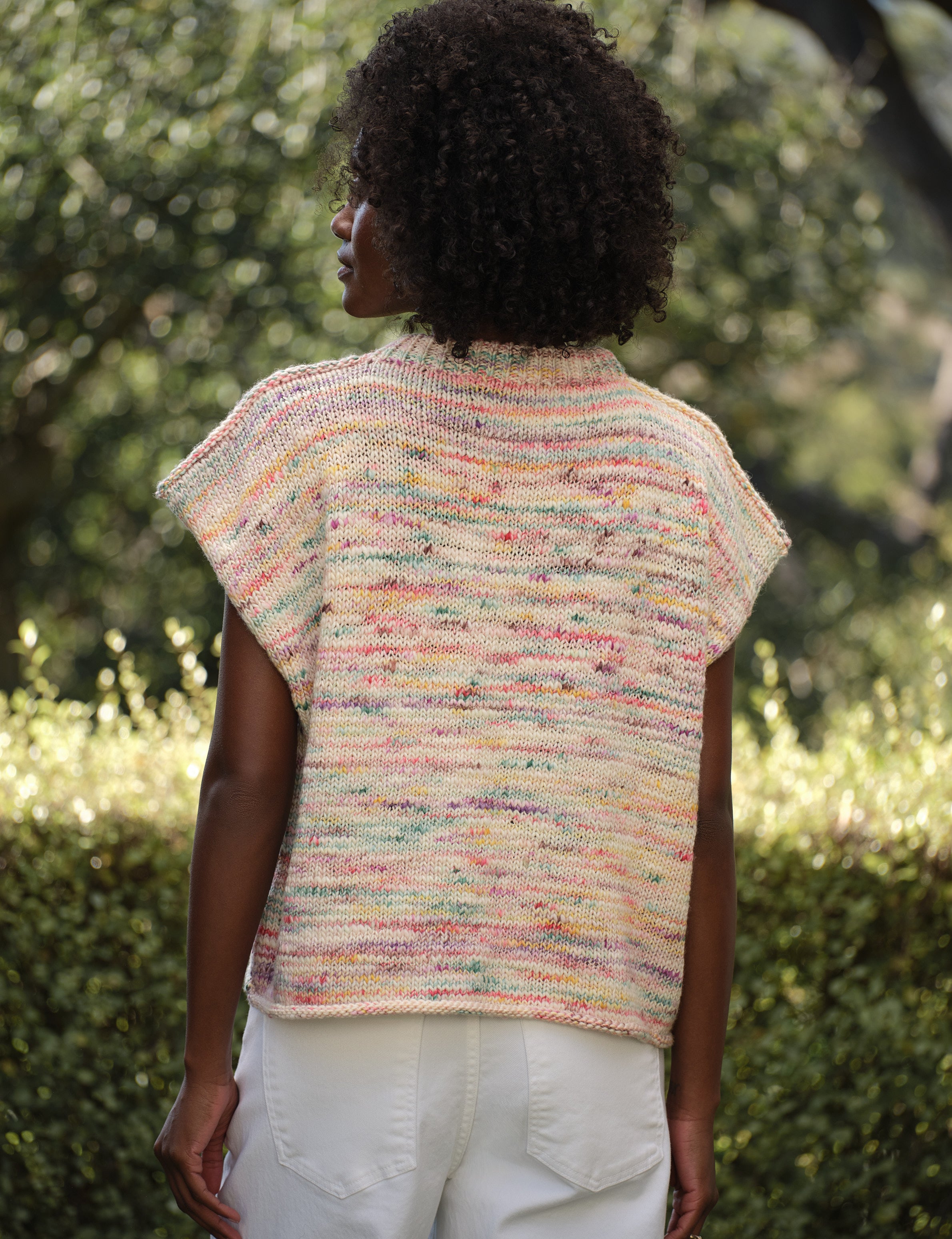 Person wearing a colorful knitted vest in an outdoor setting, alternate view