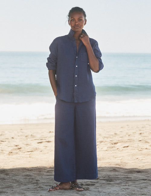 Person wearing a blue outfit standing on a beach with ocean in the background, front view