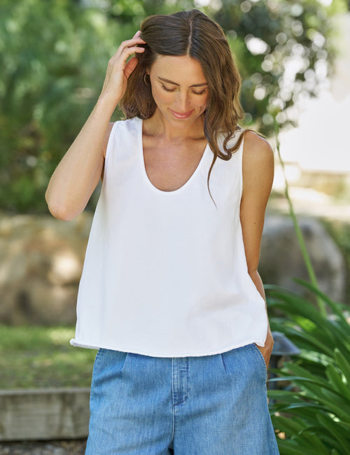 Woman wearing a white sleeveless top and blue shorts outdoors., front view