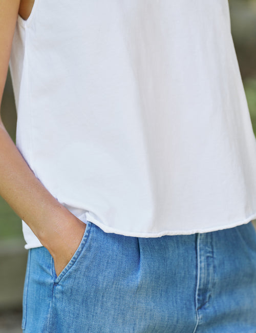 Person wearing a white top and blue jeans with a blurred background, view 3