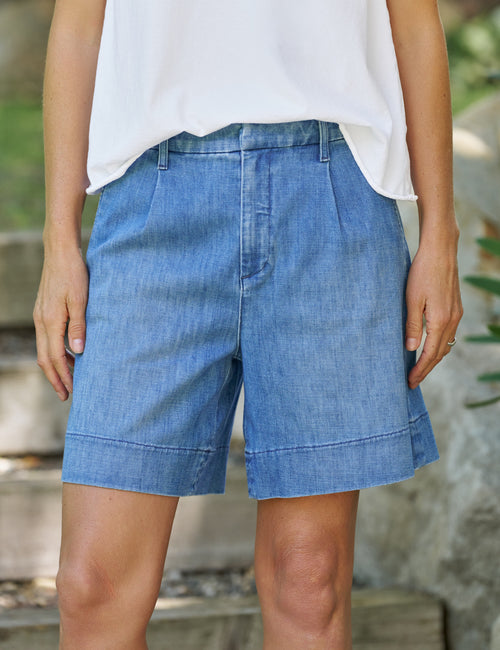 Person wearing blue denim shorts and a white top outdoors., front view
