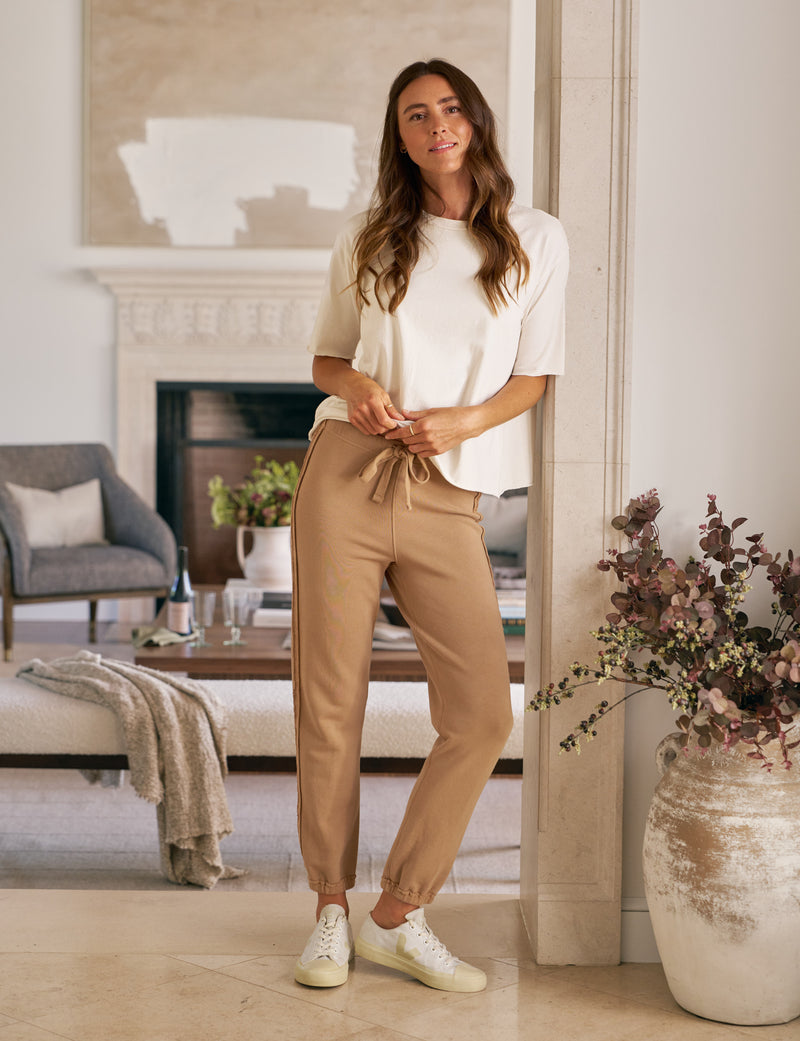 Woman in a white top and beige pants standing in a living room.