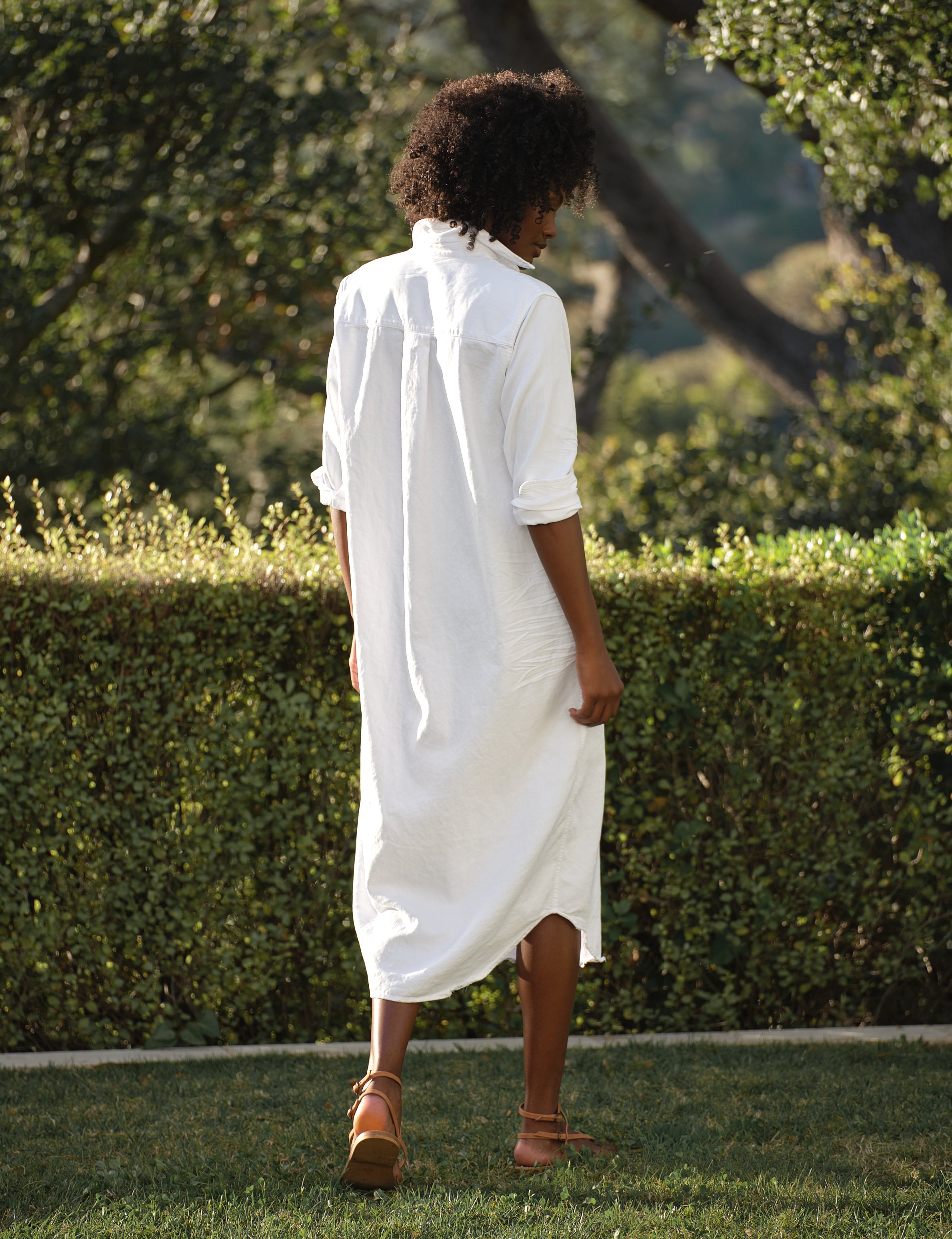 Person wearing a white dress standing in a garden with greenery, alternate view