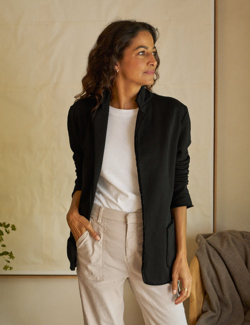 A woman is standing, wearing a black blazer, paired with a white top and beige pants., front view