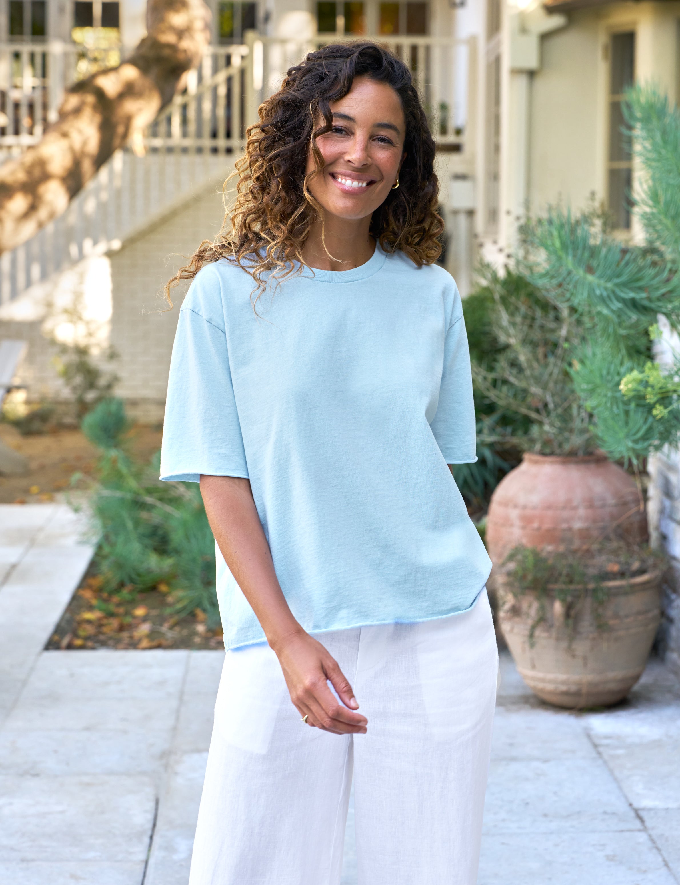 Woman wearing a light blue shirt and white pants standing outdoors.