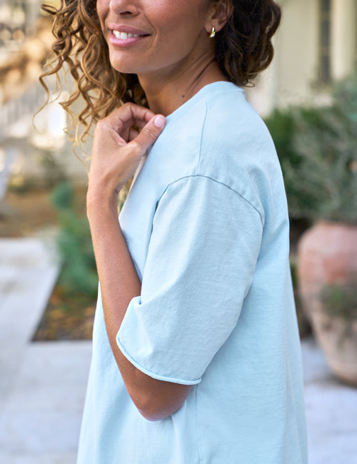 Woman wearing a light blue dress with a blurred outdoor background, view 3