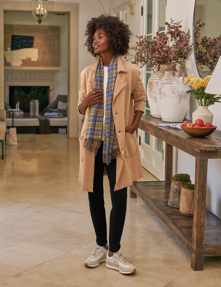 Woman in a beige trench coat with a plaid scarf standing in a living room.