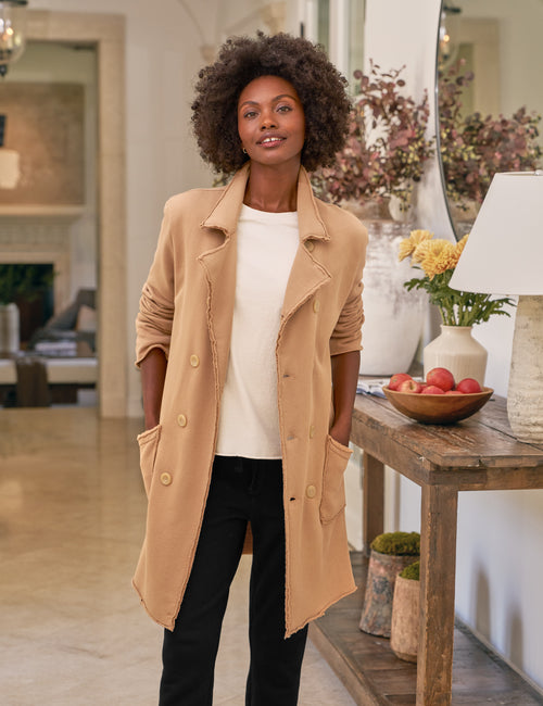 Woman wearing a beige coat in a living room setting, front view