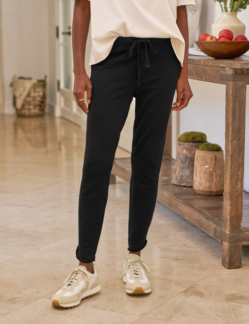 Person wearing black pants and white sneakers in a home setting, front view