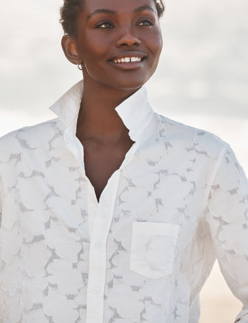 Woman wearing a white patterned shirt against a blurred natural background, view 3