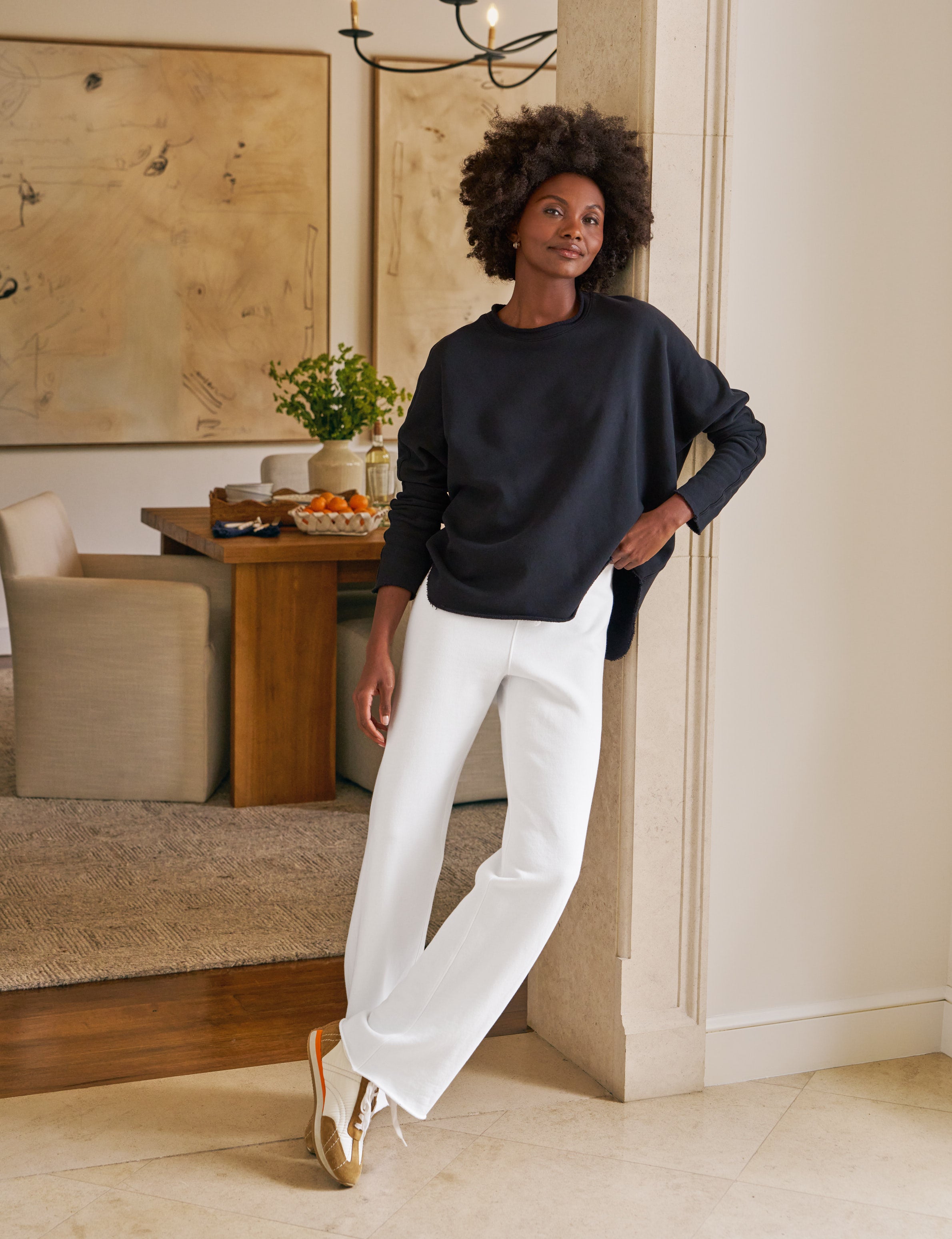 Woman in a navy sweater and white pants standing in a living room.