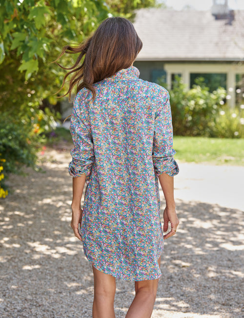 Woman in a colorful dress walking away from the camera on a gravel path with greenery and a house in the background., alternate view
