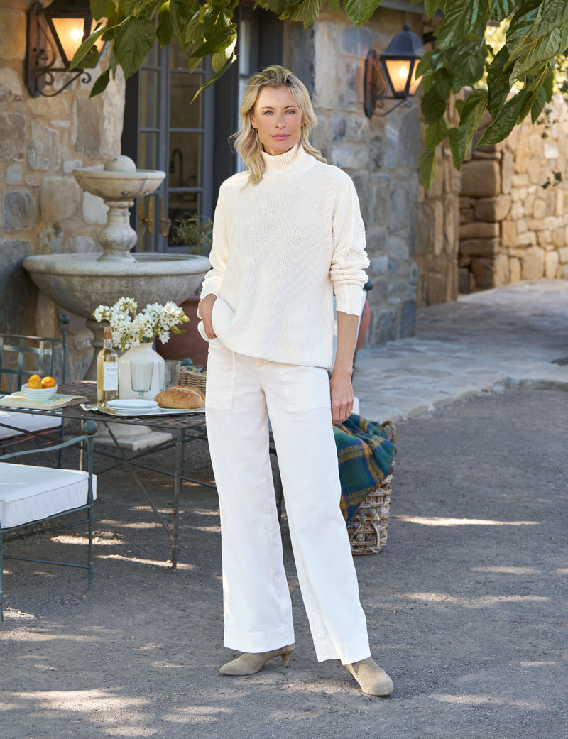 Woman in a white outfit standing outdoors near a stone building with a fountain.