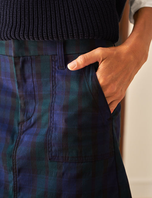Person wearing blue plaid skirt with a hand in the pocket against a neutral background, view 3