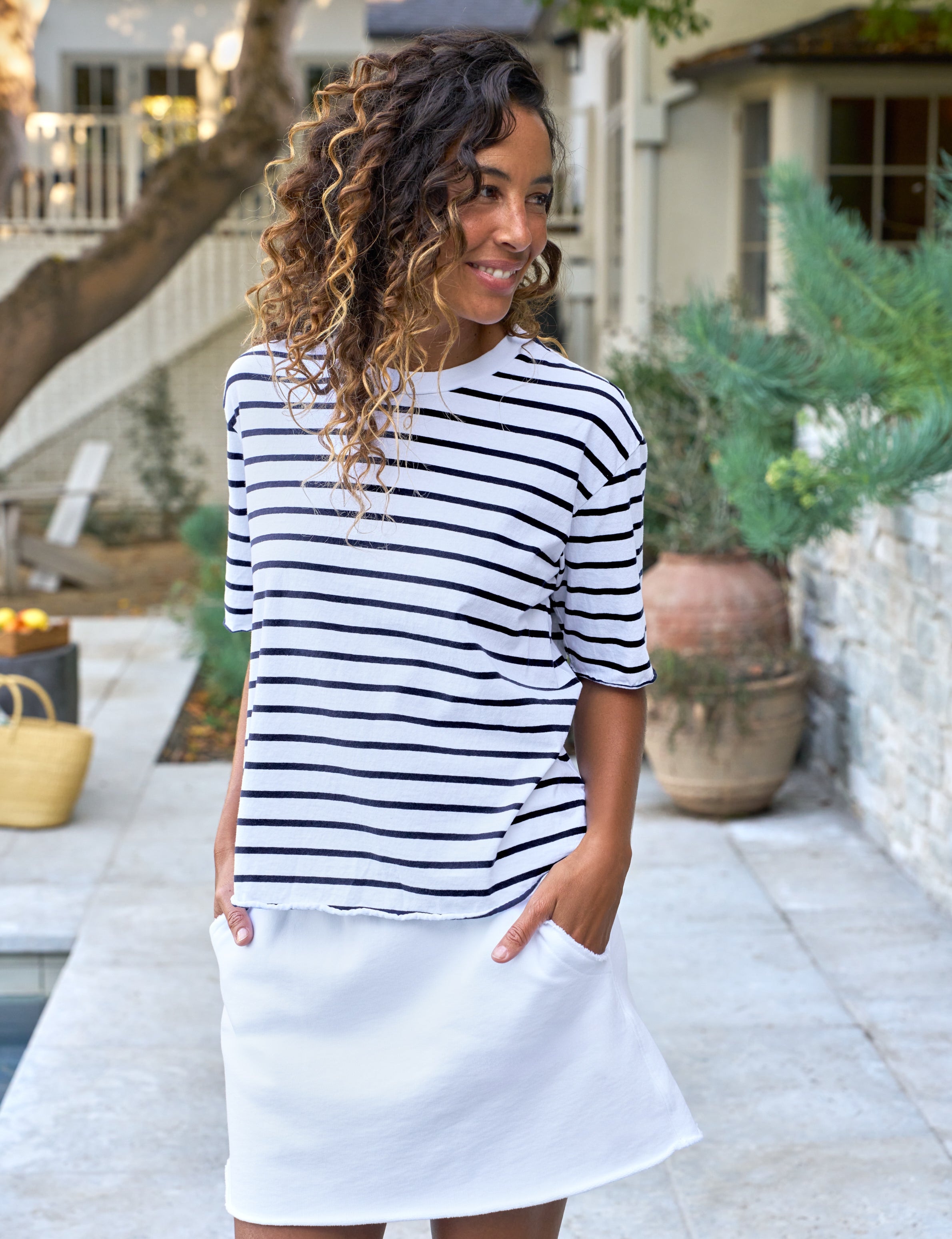 Woman wearing a navy and white striped shirt with a white skirt outdoors.
