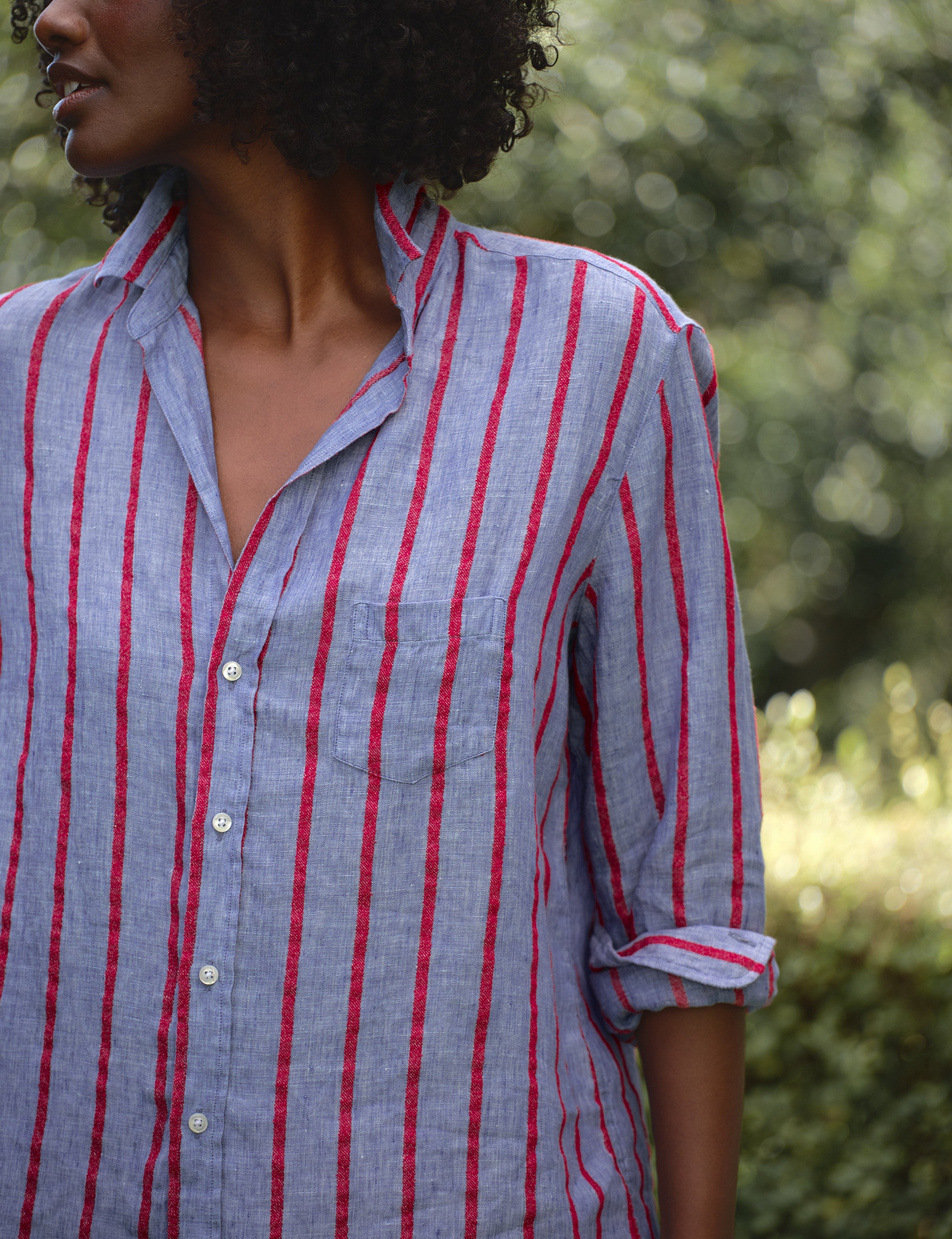 Person wearing a blue and red striped shirt with a blurred natural background, view 3
