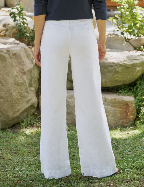Person wearing white pants standing outdoors with rocks and greenery in the background, alternate view