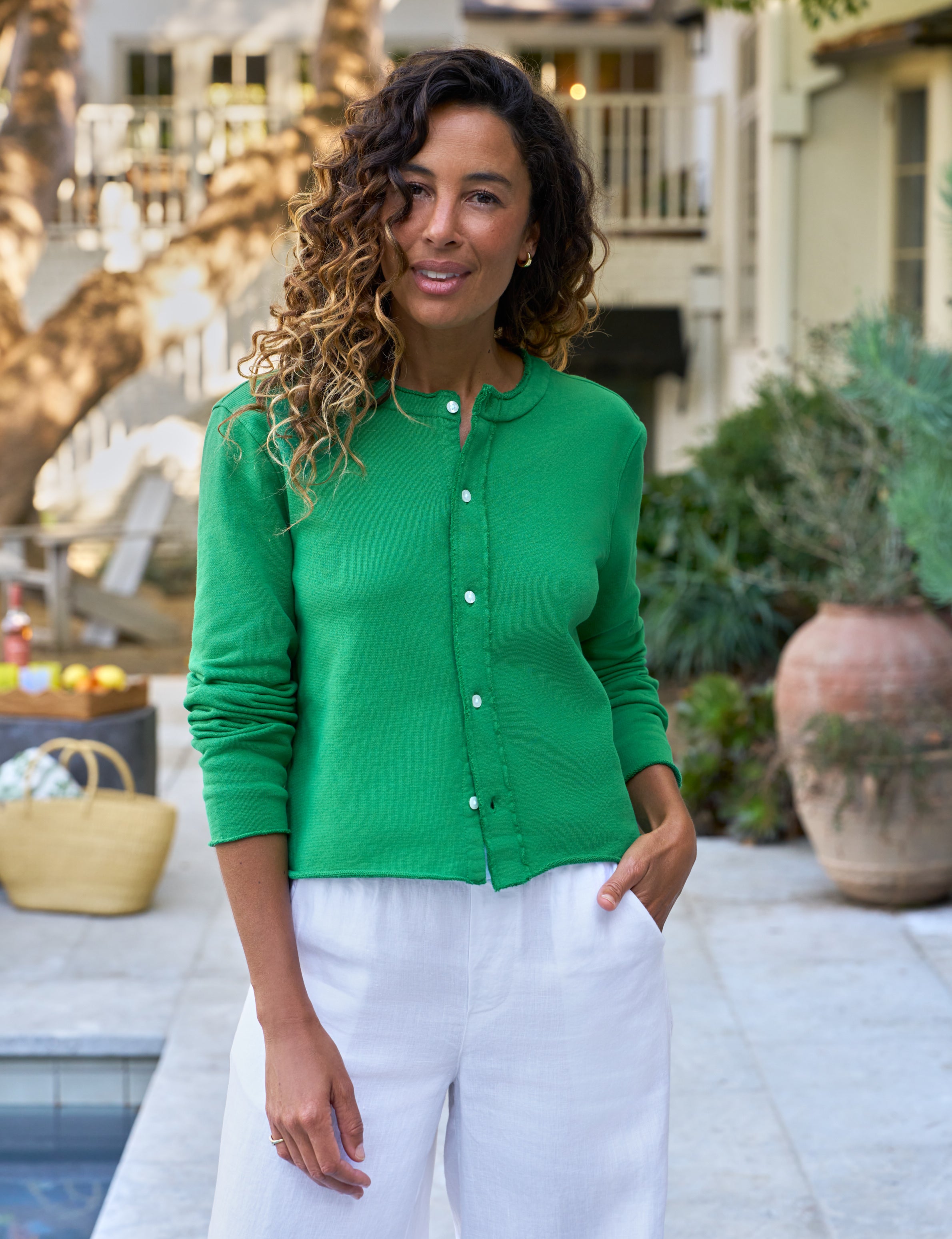 Woman wearing a green cardigan and white pants standing outdoors near a pool.