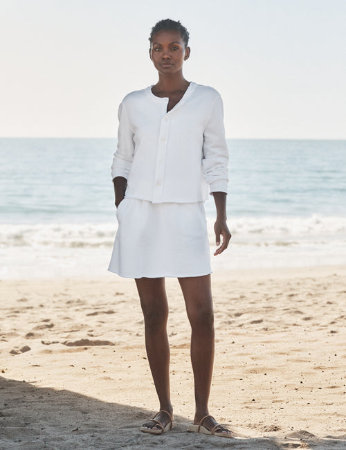 Woman in a white outfit standing on a beach with ocean in the background, view 4