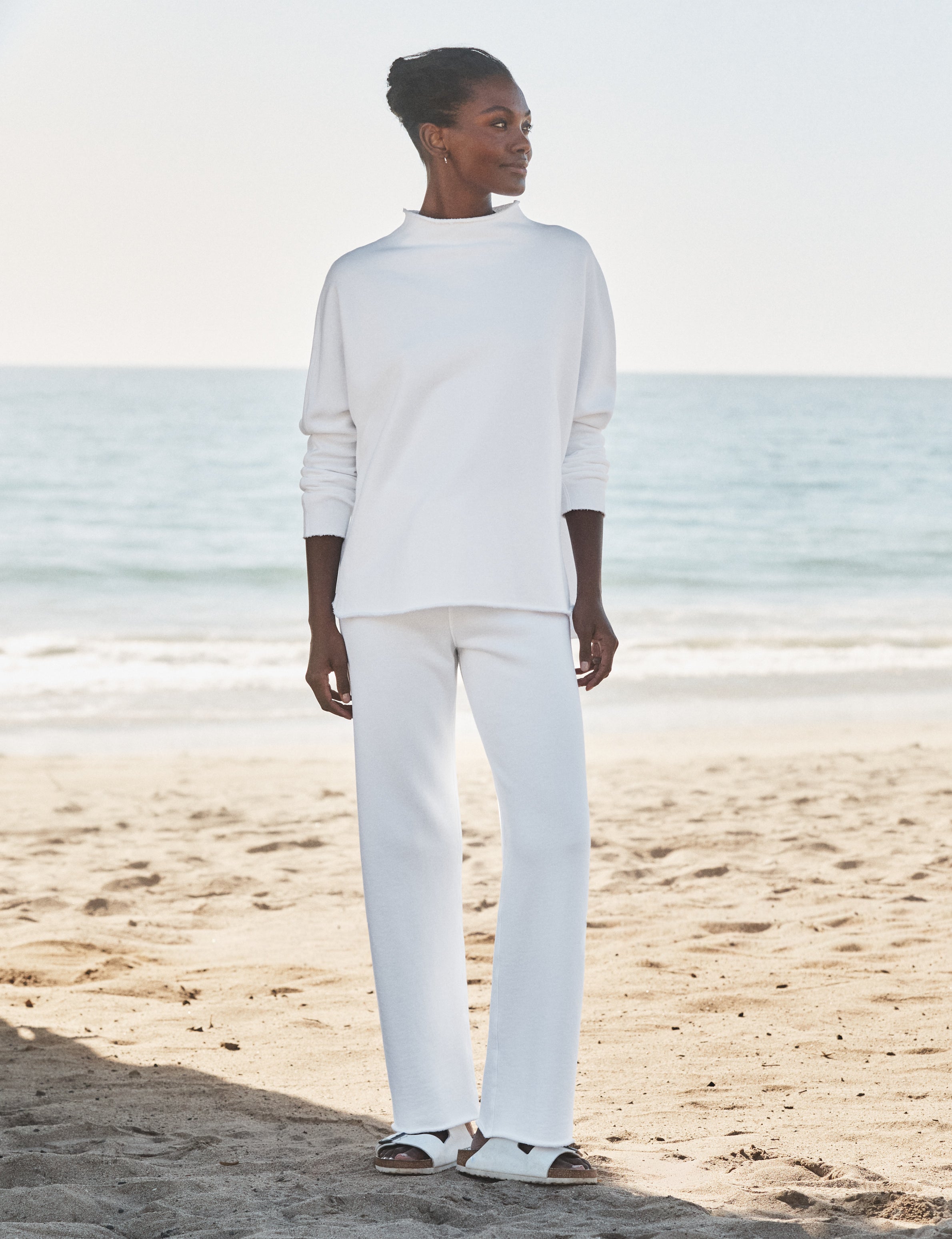 Person wearing a white outfit standing on a beach with ocean in the background, front view