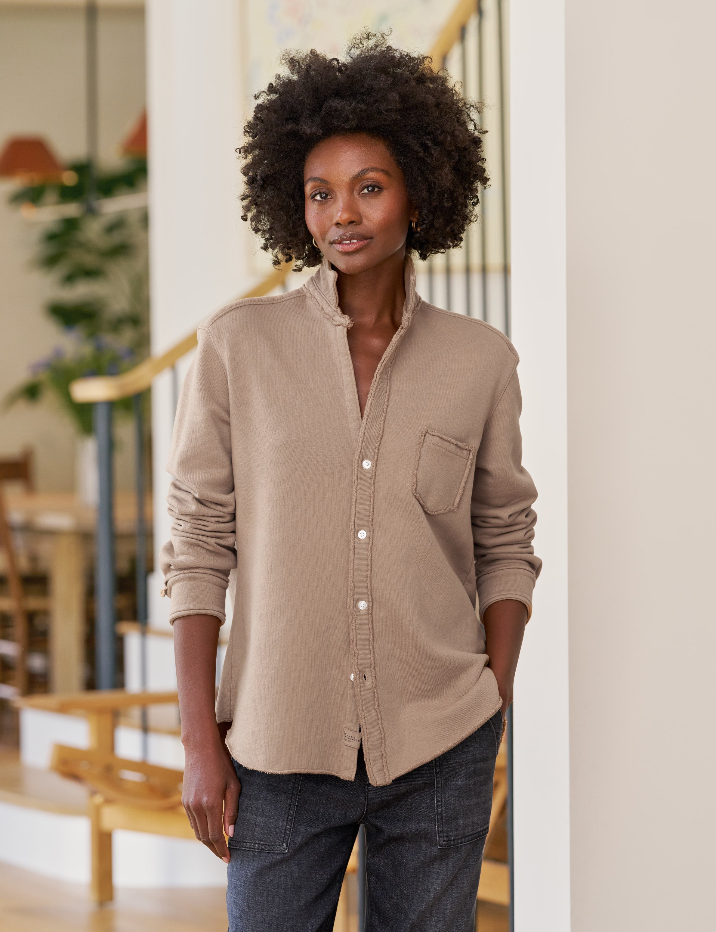 Woman wearing a beige button-up shirt and jeans indoors