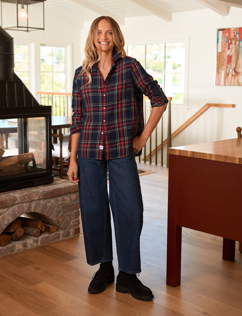 A woman stands in a bright, modern home interior wearing a red and navy plaid button-down shirt, dark blue wide-leg jeans, and black boots., view 4
