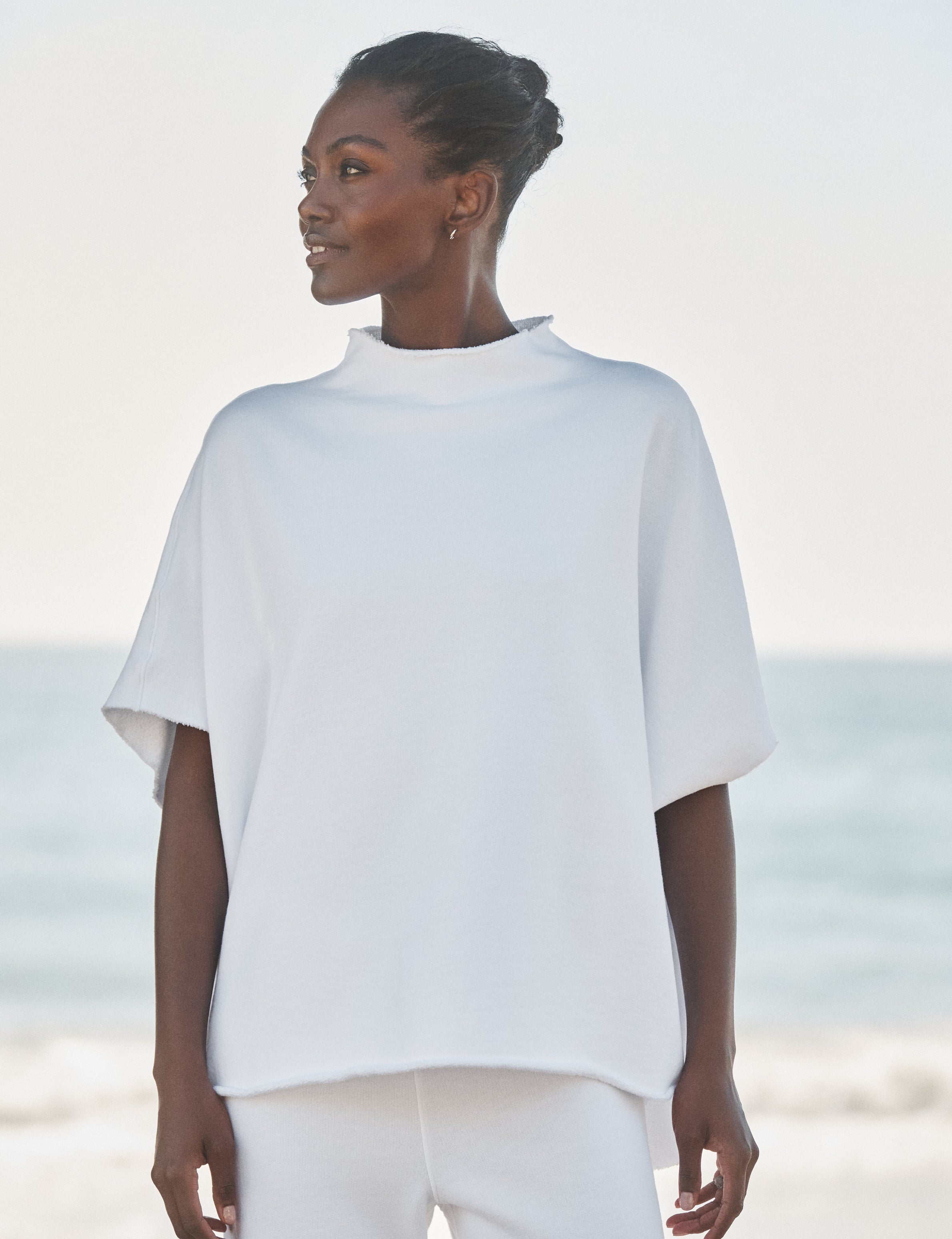 Woman wearing a white oversized capelet on a beach, front view