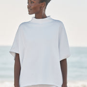 Woman wearing a white oversized capelet on a beach