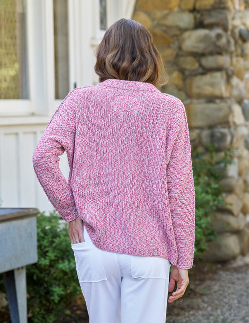 Woman wearing a pink textured sweater and white pants standing outdoors., alternate view