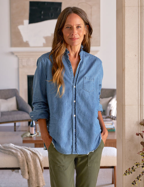 Woman wearing a blue shirt and green pants standing in a living room., front view