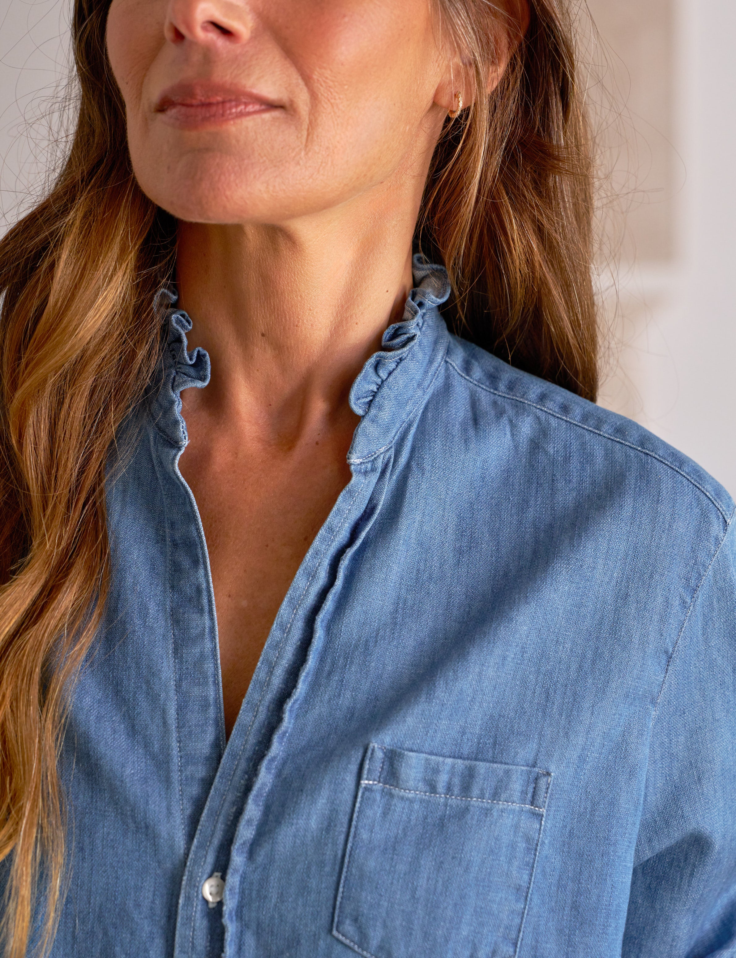 Woman wearing a blue denim shirt with a neutral background