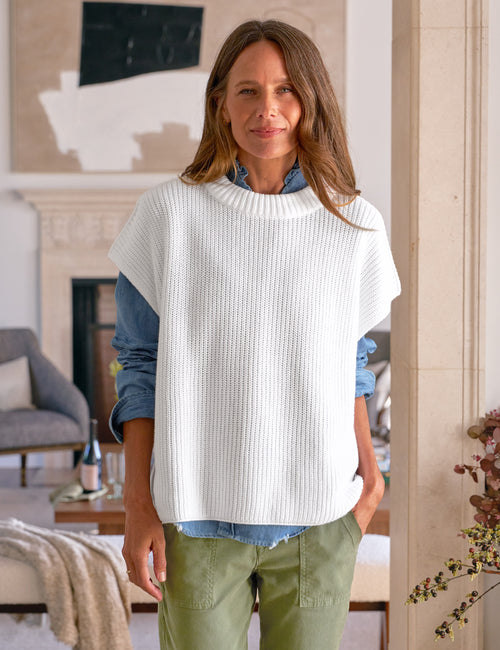 Woman wearing a white sweater over a blue shirt in a living room setting, front view