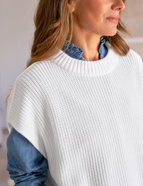 Woman wearing a white knit sweater over a blue shirt with a blurred background, view 3