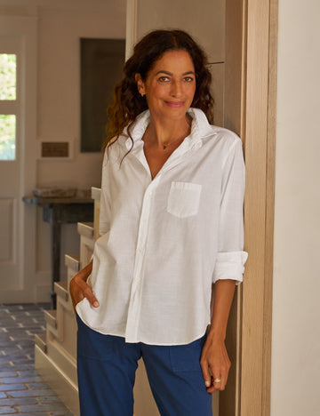 Woman wearing a white shirt and blue pants standing in a doorway.