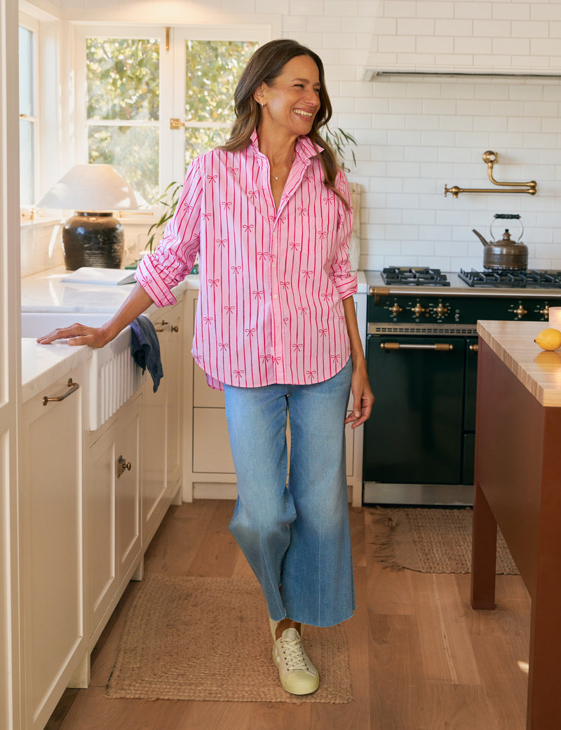 Woman in a kitchen wearing a pink striped shirt and blue jeans.