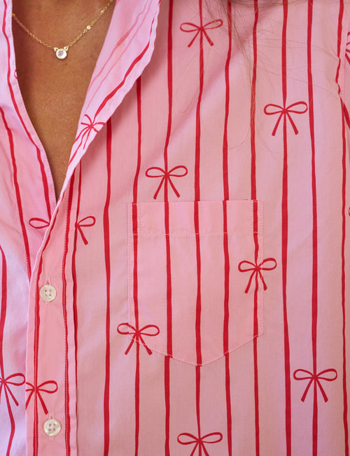 Close-up of a pink shirt with red bow patterns and gold buttons., view 3