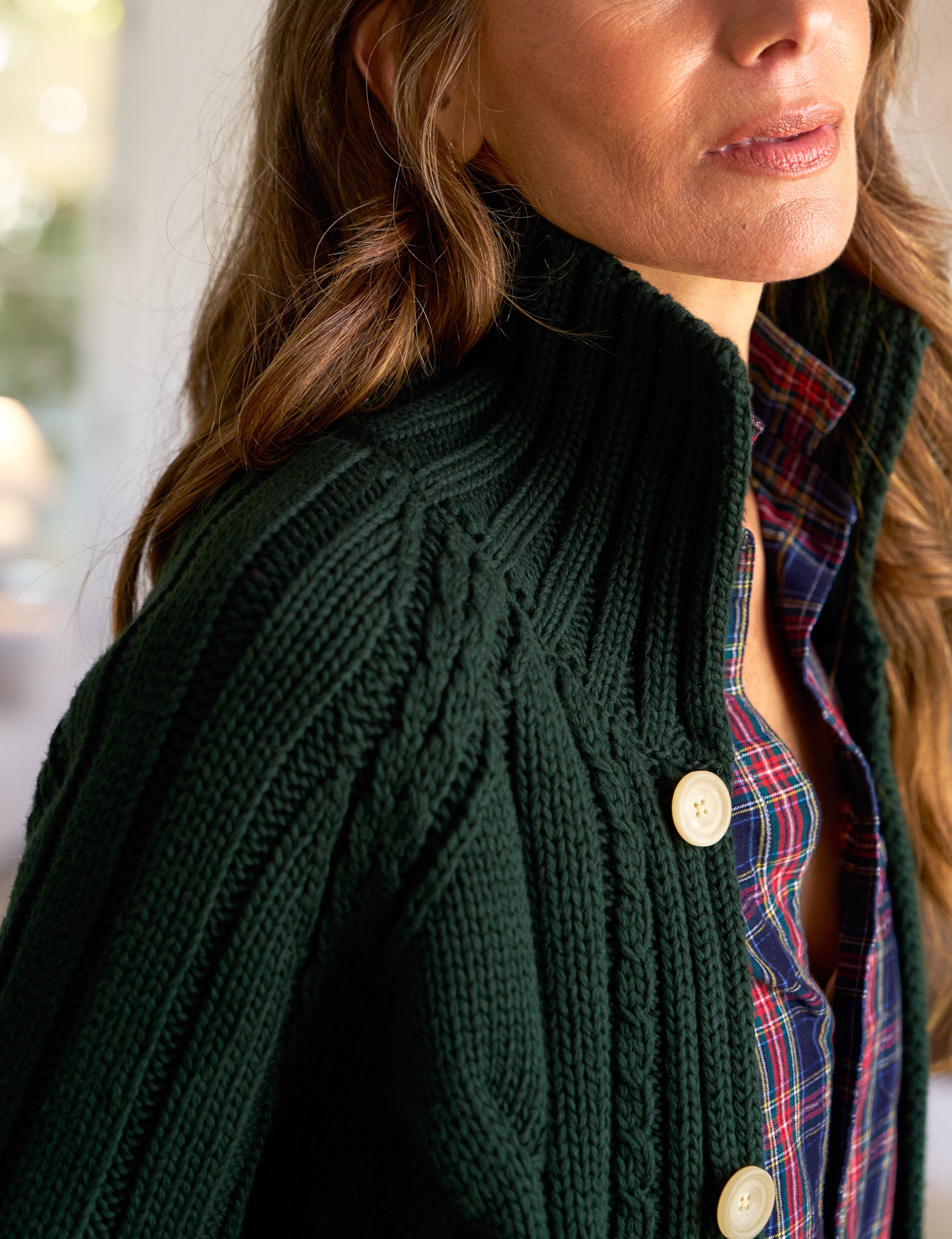 Woman wearing a dark green knitted cardigan over a plaid shirt.