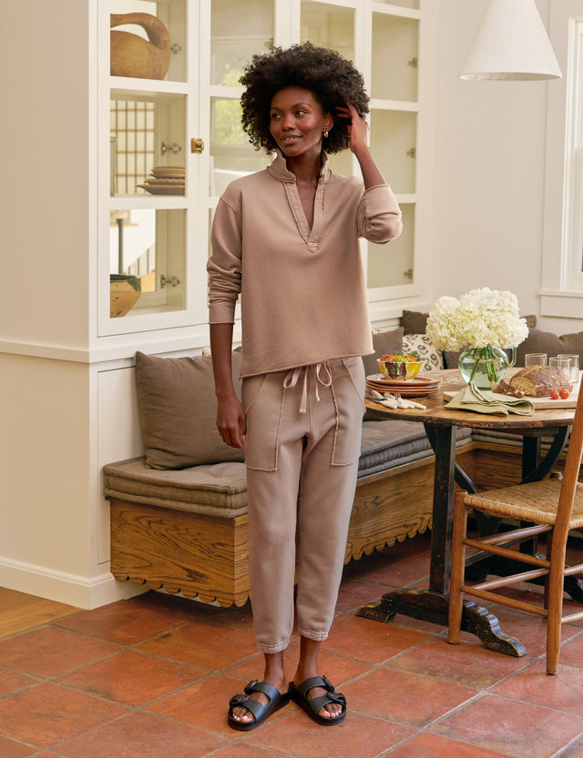 Woman in beige outfit standing in a home interior with a table and chairs.