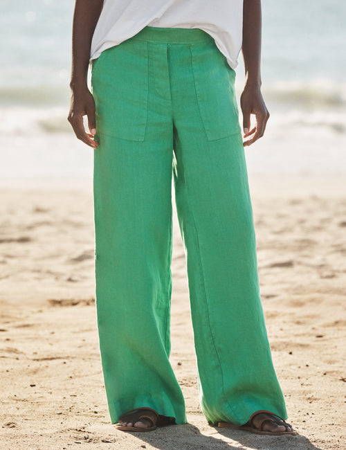 Person wearing green pants standing on a sandy beach., front view