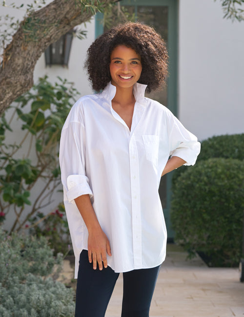 Woman wearing a white shirt and dark pants standing outdoors., front view