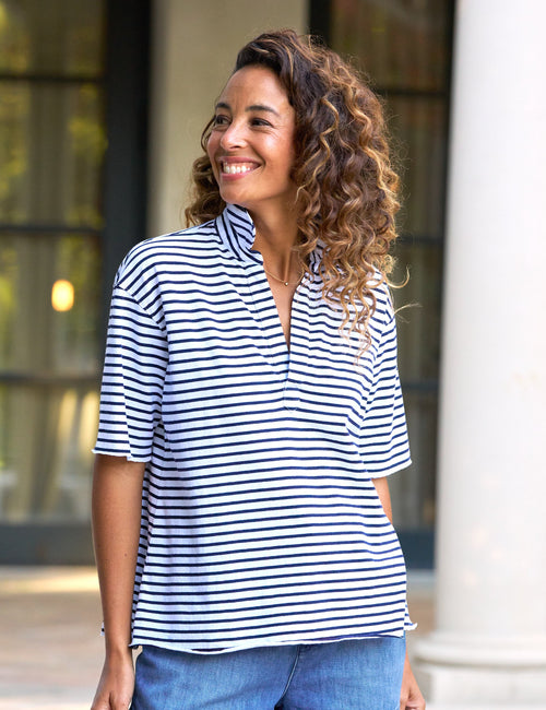 A woman wearing a navy and white striped short-sleeved henley top with a preppy v-neck., front view