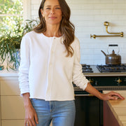 Woman standing in a kitchen wearing a white shirt and blue jeans.