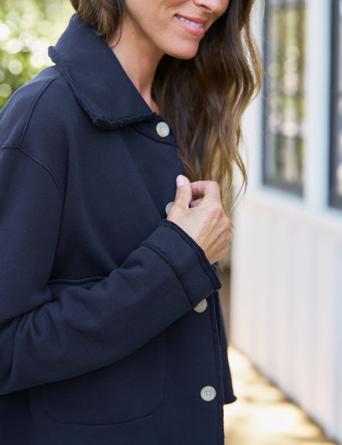 A woman wearing a dark navy blue coat with a collar and light-colored buttons, shown in a close-up outdoor shot., view 3