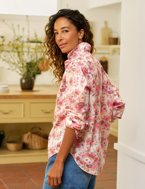 Woman in a floral shirt and denim shorts standing in a kitchen., alternate view