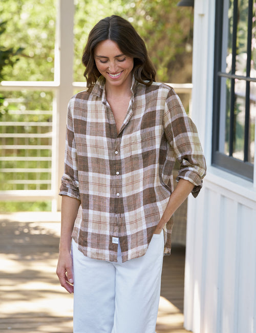 Woman wearing a plaid shirt and light pants on a porch, front view