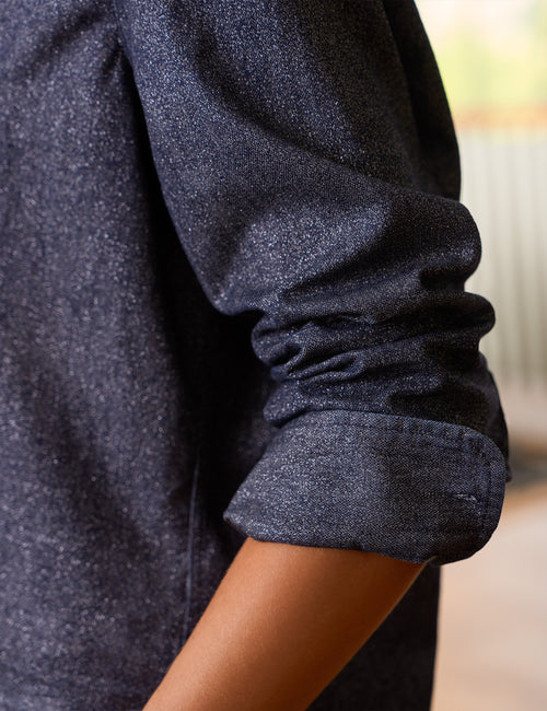 Close-up of a person wearing a dark blue glitter textured long-sleeve shirt, showing the rolled-up cuff and part of the arm., view 3