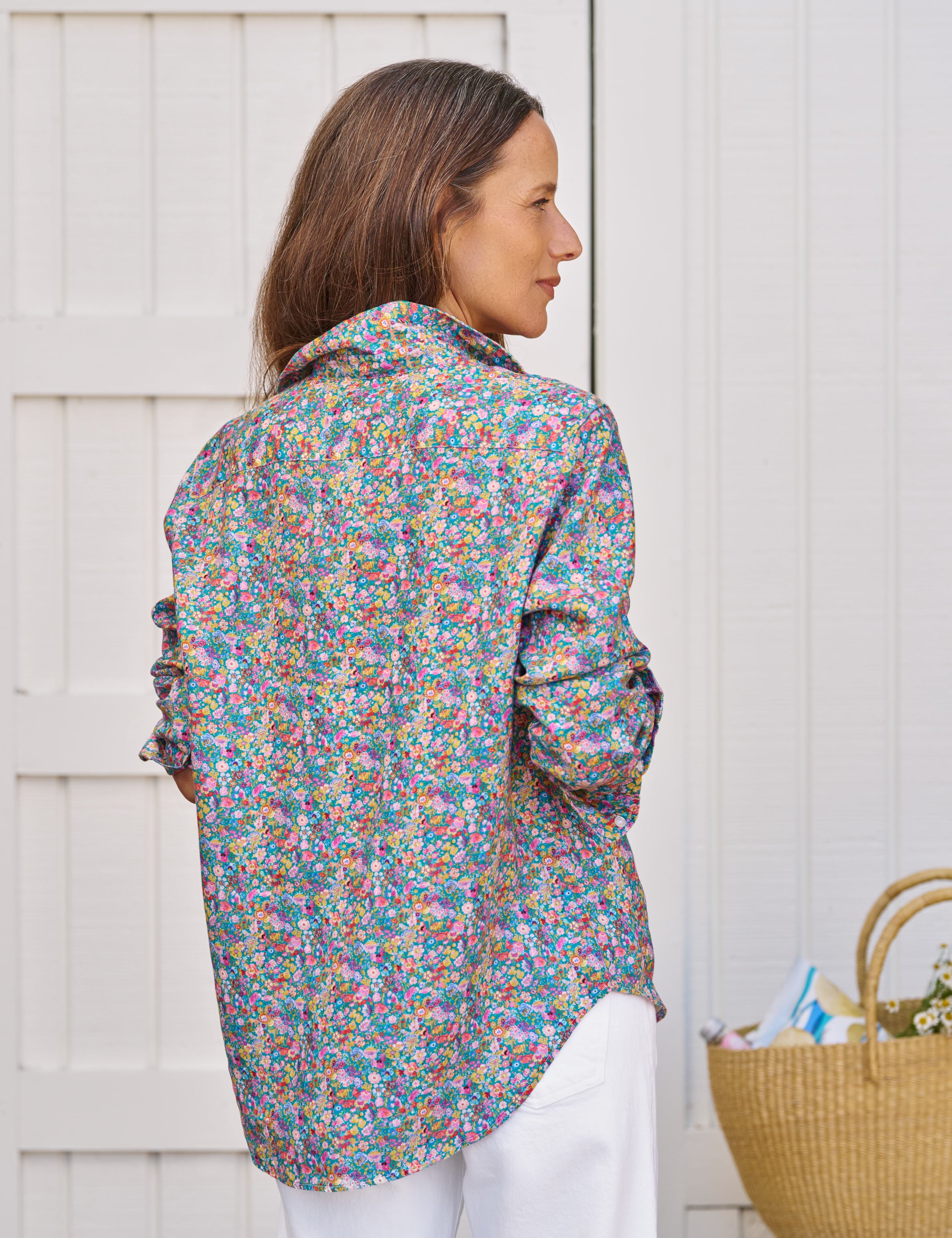 Woman wearing a colorful floral shirt standing against a white wooden background, alternate view